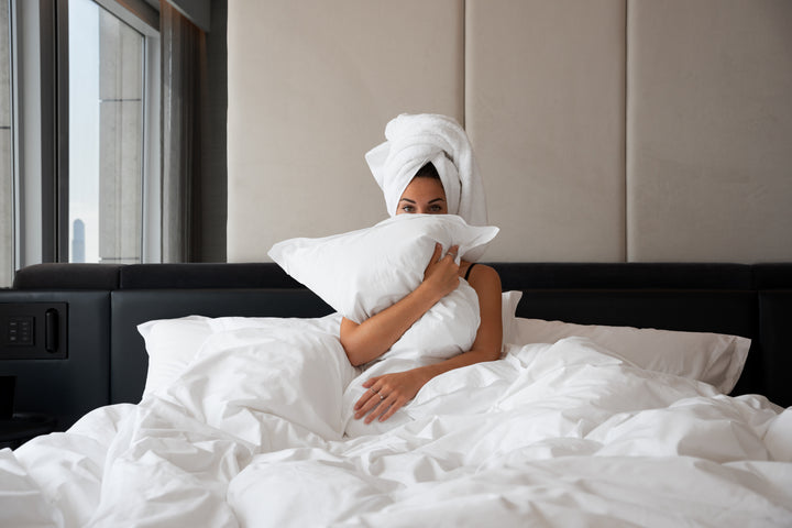 A girl lying on a bed, hugging a pillow, with a towel on her head.